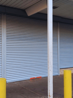 Security shutter style roll-up door installed with yellow Ballards in front